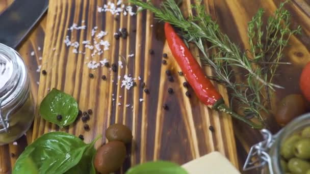 Close up vegetables pepper, tomato, onion, garlic and herbs rosemary, salt, olives for cooking food on kitchen. Trecking shot vegetables and seasoning herbs on wooden table. - Video