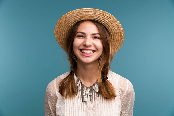 Portrait of a young happy girl in summer hat isolated over blue background, looking at camera - Foto, immagini