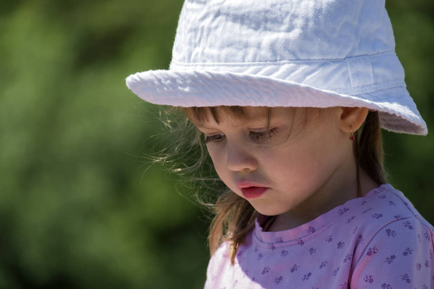 Menina bebê em um chapéu branco tristemente abaixou os olhos
 - Foto, Imagem