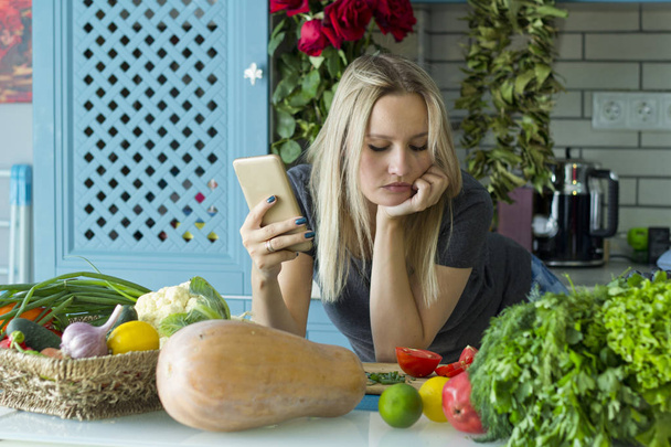 Дівчина готується здорової їжі на кухні з овочами. За допомогою смартфона шукає за рецепт. Вегетаріанська кухня. Молодий Європейського у двадцяті роки. Концепція здорове харчування. - Фото, зображення