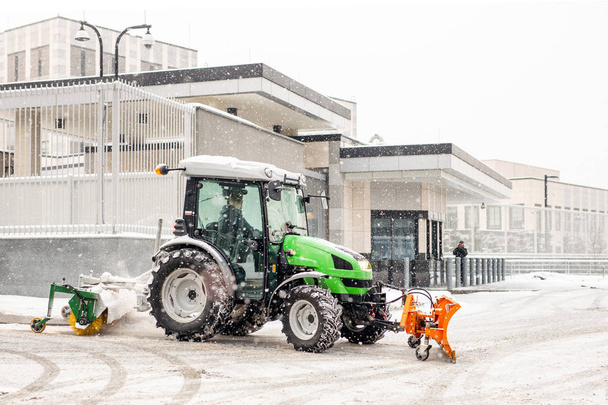 Trator com escova e colher limpeza de neve na rua da cidade e estacionamento durante a queda de neve pesada no inverno
 - Foto, Imagem