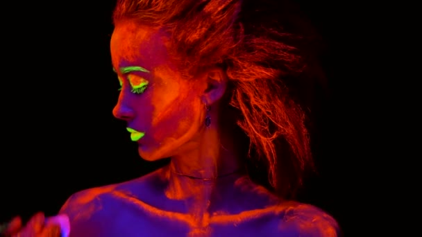 Une belle jeune fille sexy avec de la peinture ultraviolette sur son corps regardant une main d'artiste avec un pinceau, peignant son épaule. Jolie femme avec bodyart lumineux dans la lumière de la lampe noire
. - Séquence, vidéo