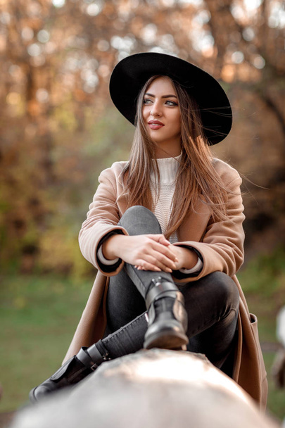 bela mulher de moda em chapéu preto sentado na árvore
 - Foto, Imagem