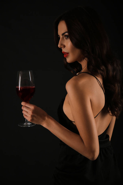 Beautiful young woman with glass of wine on dark background - Foto, afbeelding