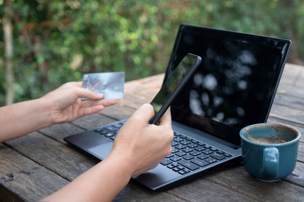 Okostelefon és hitelkártyák a kezében laptoppal és kávéval a fa asztalon. - Fotó, kép