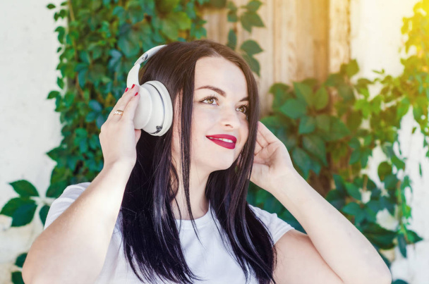 黒髪のかわいい笑顔の女の子は白のワイヤレスヘッドホンで音楽を聴きます。音楽のスタイル。ソフトな音楽。自立した女性 - 写真・画像