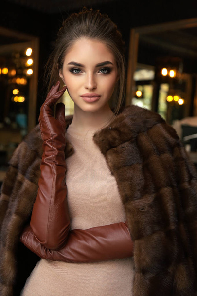 fashion outdoor photo of beautiful woman with dark hair in luxurious fur coat and leather gloves posing in restaurant  - Φωτογραφία, εικόνα
