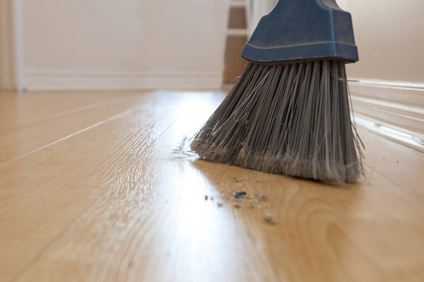 Σκούπα σαρώματα προέρχονται περίοδο με σκόνη και το ρύπο στο ξύλινο πάτωμα με αντίγραφο χώρου - Φωτογραφία, εικόνα