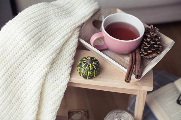 Knitted, warm sweaters, a cup of hot tea, autumn decor, a book, a pumpkin on a wooden chair. Cozy, autumn decor. Autumn interior, sofa. Fall. Winter. - Photo, Image