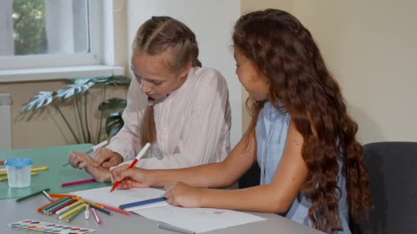Two school friends talking while drawing together at art class lesson - Imágenes, Vídeo