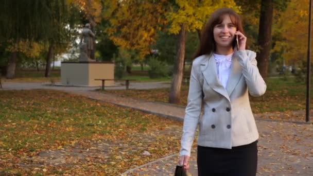 hermosa mujer de negocios hablando por teléfono móvil, mujer feliz caminando por el parque de otoño y sonriendo
 - Metraje, vídeo
