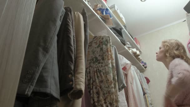 Beautiful girl smiles and goes through hangers with clothes in her dressing room. - Footage, Video