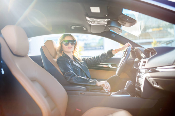 Image of side of blonde in black glasses sitting behind wheel in car - Fotó, kép