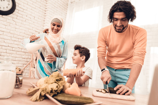 Happy Arabian Family Cooking Food in Kitchen. Muslim Family. Smiling Boy. Young Arabian Woman. Modern Kitchen at Home. Man Using Kitchenware. Young Family. Wooden Table in Kitchen. Food on Table. - Photo, image