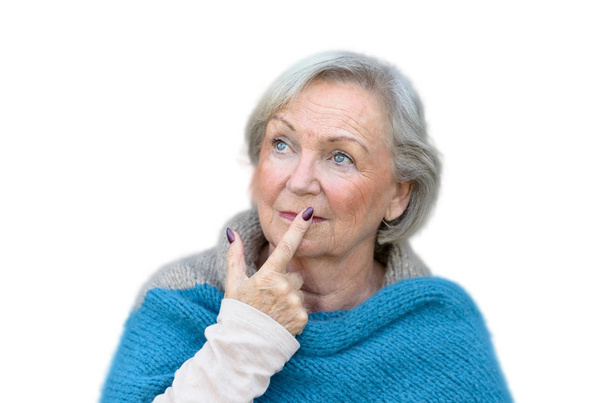 Ragionevole donna anziana elegante guardando in aria con il dito alle labbra e un'espressione contemplativa contro un muro grigio
 - Foto, immagini