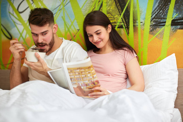 Young couple in love in morning in bed together reading and eating  - Foto, immagini