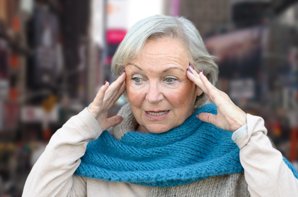 Запутавшаяся и сбитая с толку пожилая леди, держащая руки за виски, смотрит в сторону, концептуально о начале деменции или болезни Альцгеймера
 - Фото, изображение