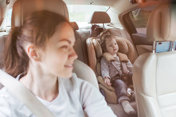 The child in a safety seat near to mother who sits on forward sitting of the car. Baby in a child car seat. safe transportation of children. family travels - Foto, imagen