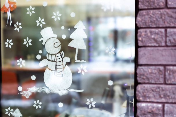 Магазин-окно украшено временным рисунком снеговика и рождественской елки из искусственного снега. Новогодние и рождественские праздники
 - Фото, изображение