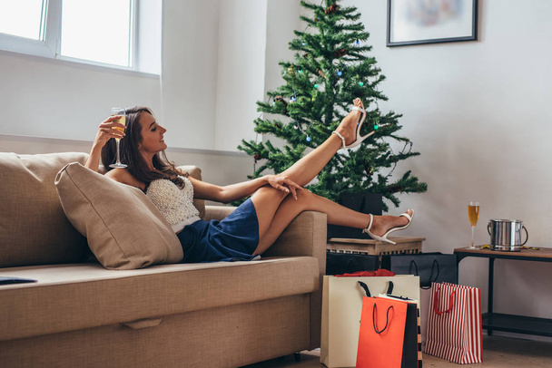 Woman siting by the christmas tree and taking a present out of shopping bag - Foto, Imagen