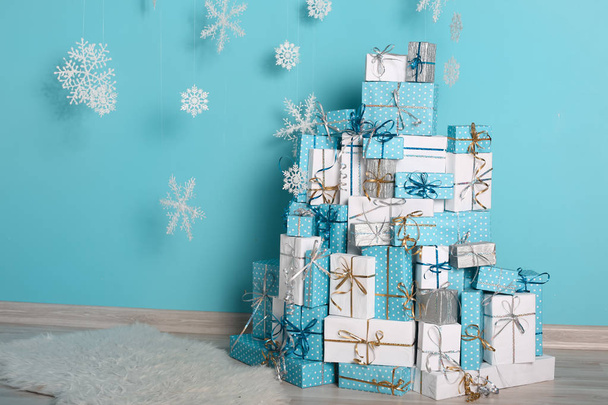 Χριστούγεννα copyspace εσωτερικό και διακοσμήσεις. Νιφάδες χιονιού και δώρο κουτιά με φιόγκο μπροστά από τυρκουάζ τοίχο τοίχο στη σύγχρονη αίθουσα χειμερινών διακοπών. Καρτ ποστάλ Χριστούγεννα φόντο. - Φωτογραφία, εικόνα