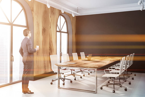 Boční pohled na moderní kancelářské setkání interiér pokoje s černými zdmi, dlážděnou podlahou a dlouhý dřevěný stůl s bílými židlemi. Obchodník s kávou. Tónovaný obrázek - Fotografie, Obrázek