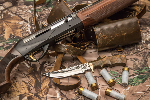 escopeta, cuchillo cazador, cartuchos y cinturón de municiones en el fondo del camuflaje
 - Foto, imagen