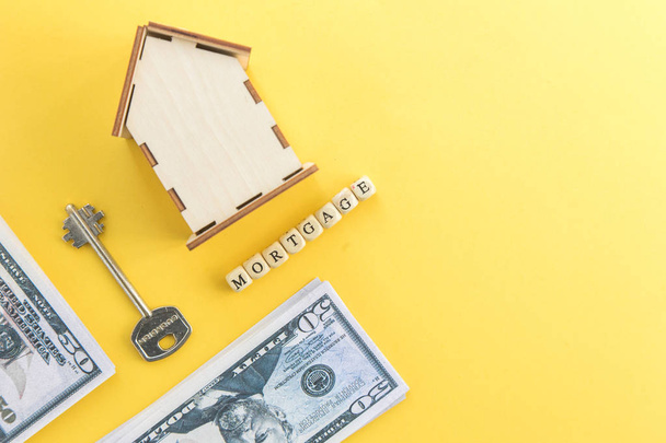 mortgage, loan and home purchase. Model of house, dollar bills, key on white and yellow isolated background. Free space for text, flat layout - Φωτογραφία, εικόνα