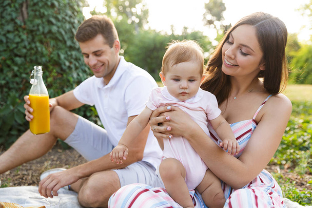 Pretty young family with little baby girl spending time together at the park, having a picnic - Фото, зображення
