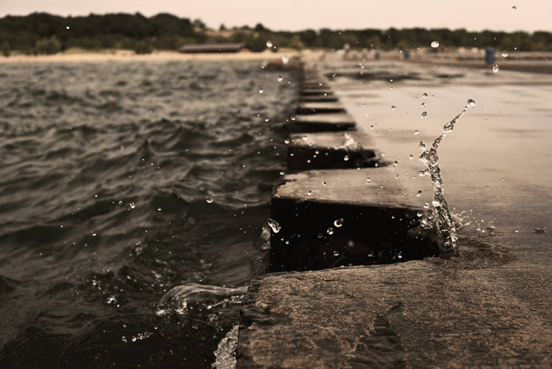 De plons van golf op steiger pier met metalen bolders. Water spatten tijdens het bewolkte weer. Splash bevroor over de pier. USA, staat Michigan, Lake Michigan. - Foto, afbeelding