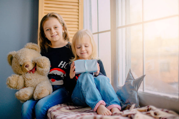 two little sisters sitting near window with gifts - Foto, afbeelding
