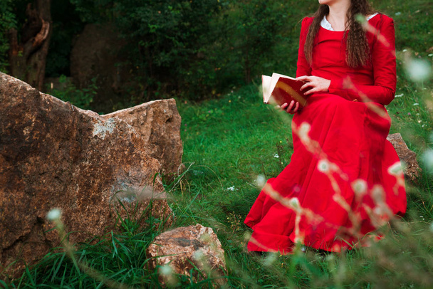 girl in red historical dress reading a book in the park - Photo, Image