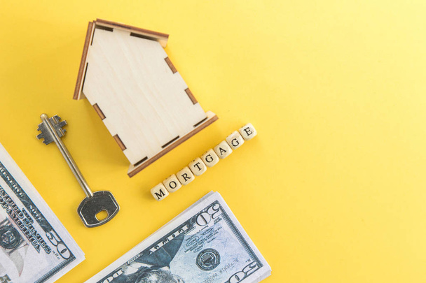 mortgage, loan and home purchase. Model of house, dollar bills, key on white and yellow isolated background. Free space for text, flatlay - Φωτογραφία, εικόνα