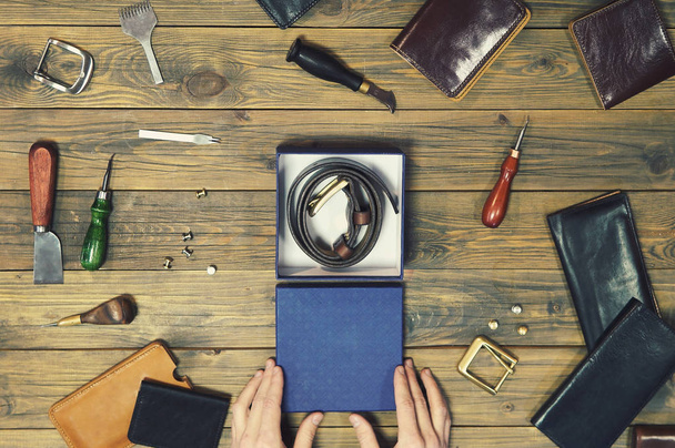 hands put a new leather wallet in a gift box. conceptual image of a gift to a man. composition of different hand made leather man accessories on wooden background - Photo, Image