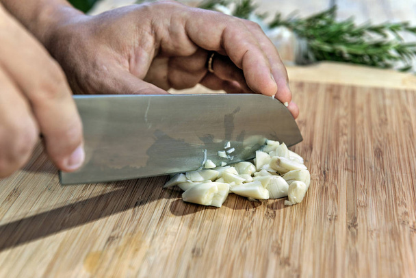 Mãos do cozinheiro cortando alho com faca na tábua de corte
 - Foto, Imagem