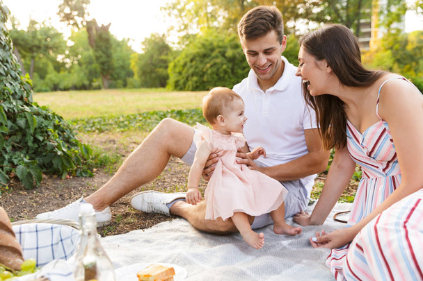 Szép fiatal család kis baba lány együtt tölteni az időt a parkban, birtoklás egy piknik - Fotó, kép