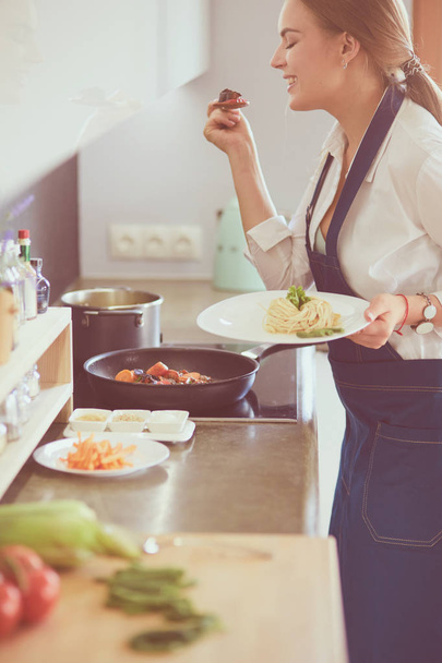 Nuori nainen seisoo lieden ääressä keittiössä - Valokuva, kuva