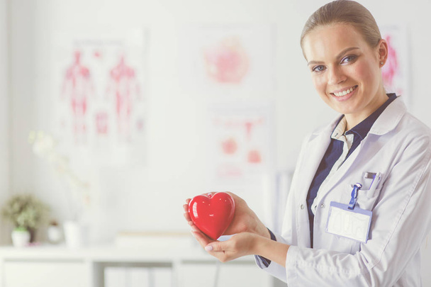 Young woman doctor holding a red heart, standing on hospital background - Foto, Bild