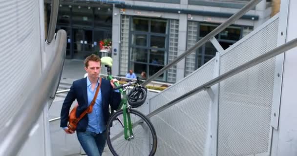 Young businessman carrying his bicycle upstairs 4k - Materiał filmowy, wideo