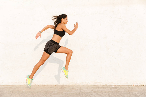 Full length image of athletic woman 20s in sportswear working out and running along wall - Photo, Image