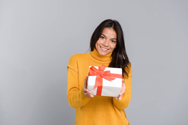 Image of a happy excited woman posing isolated over grey wall background holding box surprise present. - 写真・画像