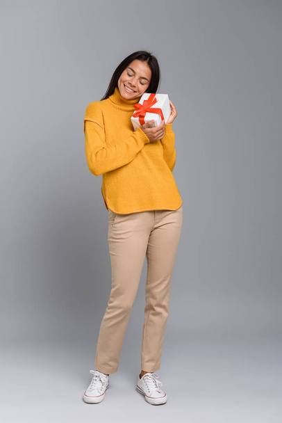 Image of a happy excited woman posing isolated over grey wall background holding box surprise present. - Foto, afbeelding