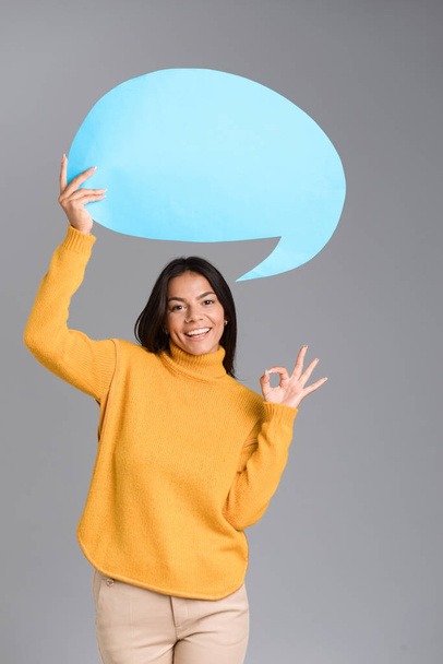 Image of a happy woman posing isolated over grey wall background holding speech bubble showing okay gesture. - Foto, Imagen