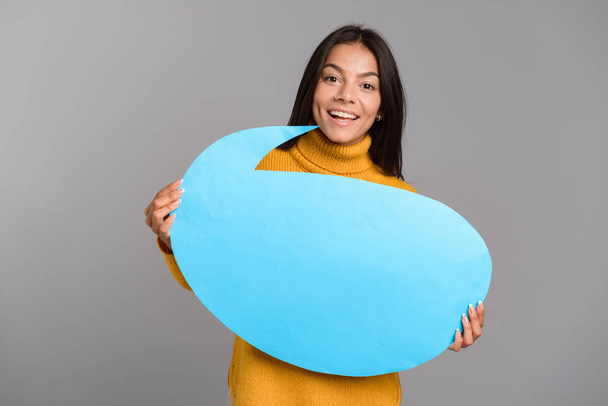 Image of a happy woman posing isolated over grey wall background holding speech bubble. - Photo, Image