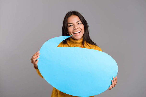 Image of a happy woman posing isolated over grey wall background holding speech bubble. - Photo, Image