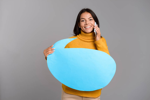 Image of a happy woman posing isolated over grey wall background holding speech bubble talking by phone. - Foto, afbeelding