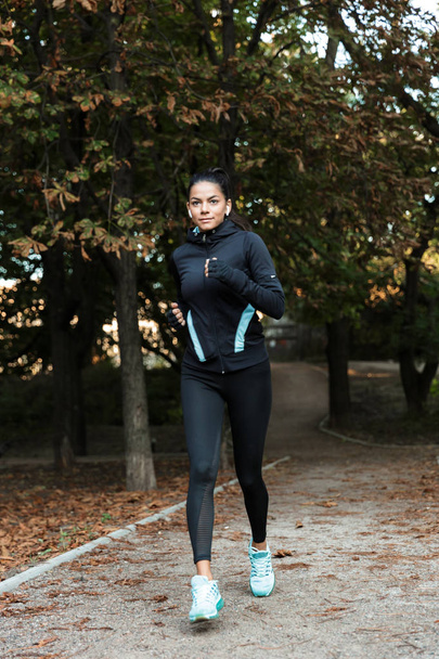 Concentrated young fitness woman jogging at the park, listening to music with earphones - Fotoğraf, Görsel
