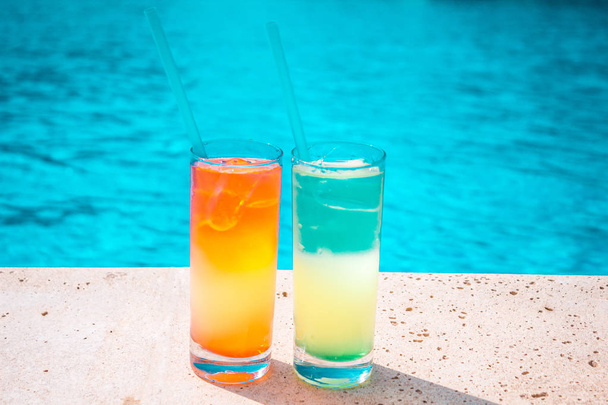 zwei bunte tropische Cocktails auf dem Hintergrund des Pools. Exotische Sommerferien. Farbcocktails auf dem Hintergrund des Wassers. - Foto, Bild