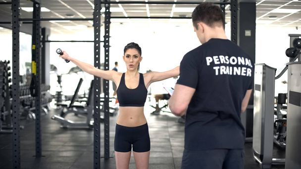 Active woman doing exercise with dumbbells during workout with personal trainer - Zdjęcie, obraz