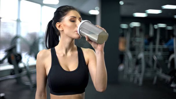 Sporty woman drinking protein shake after workout, muscle gain nutrition, health - Foto, afbeelding